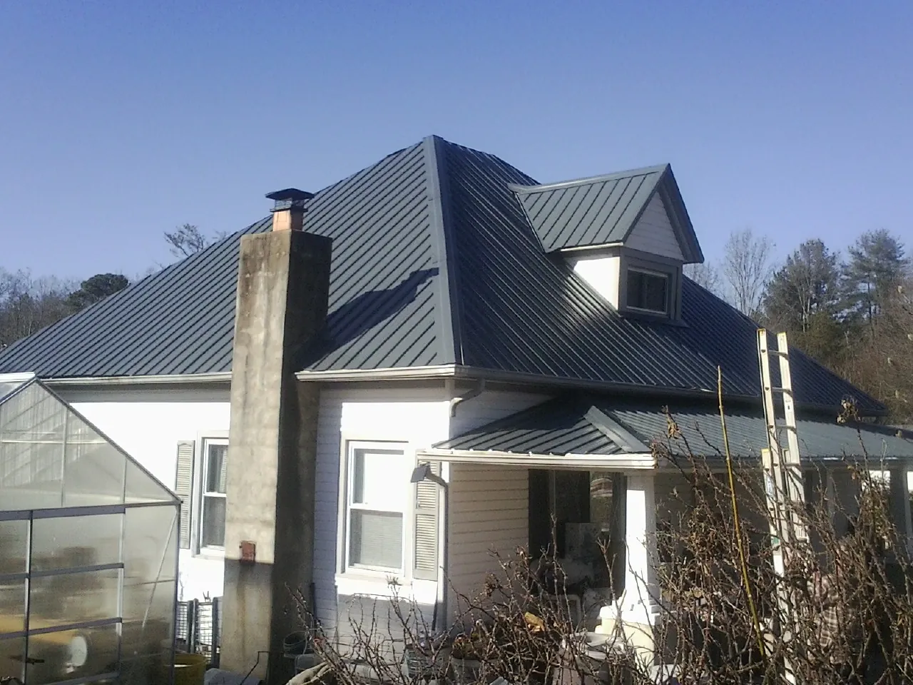 Dark blue standing seam metal roof on a white farmhouse with dormer — Slate & Tile Roof Repair by Roofing Brothers in Syria