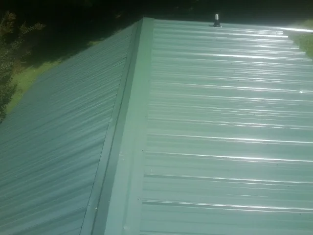 New green metal panels meeting at the ridge of a roof — Flat Roof Repair work by our crew in Syria