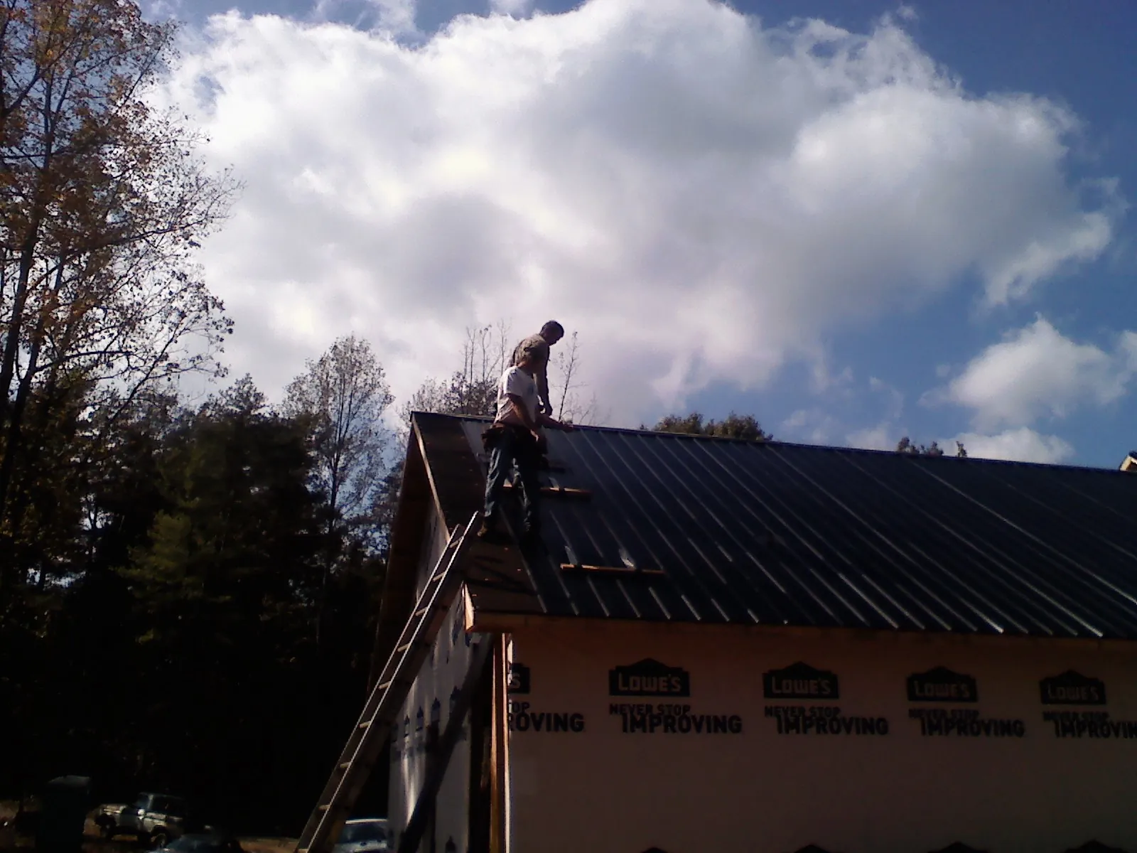 Roofer fastening dark metal panels high against a cloudy sky, from a Roof Inspection job in Syria