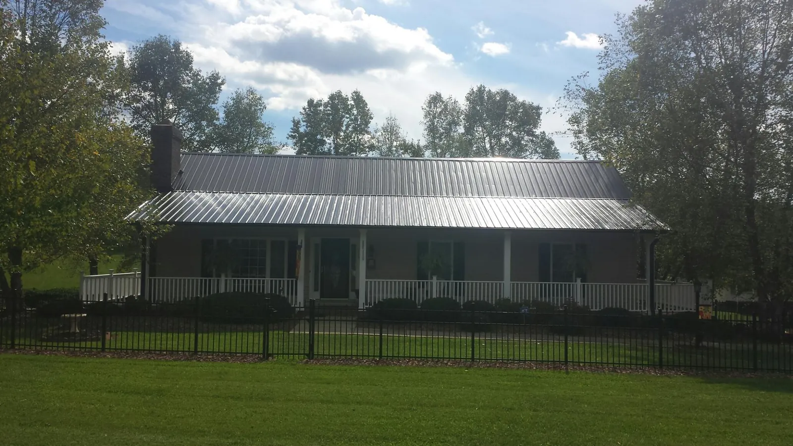 Gray metal roof on a brick ranch with a full width front porch — Gutter Guard Installation work by our crew in Syria