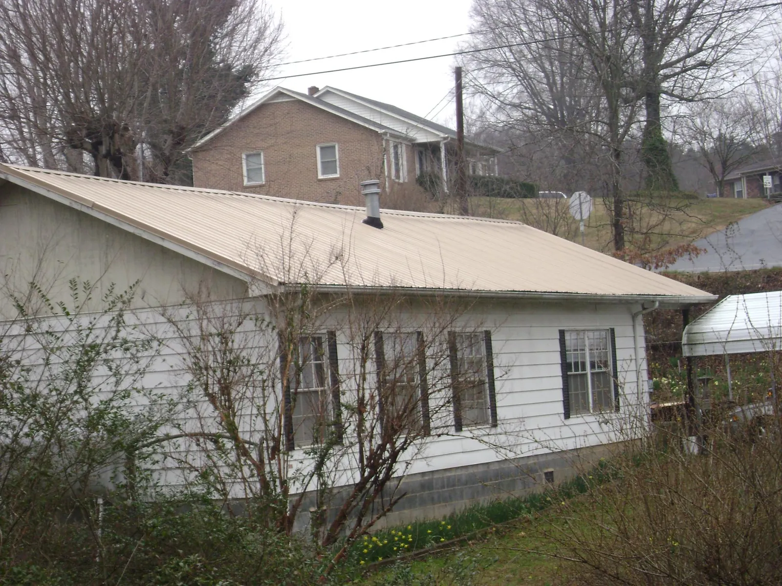 Tan metal roof on a white sided house set into a hillside — Commercial Roofing by Roofing Brothers in Syria