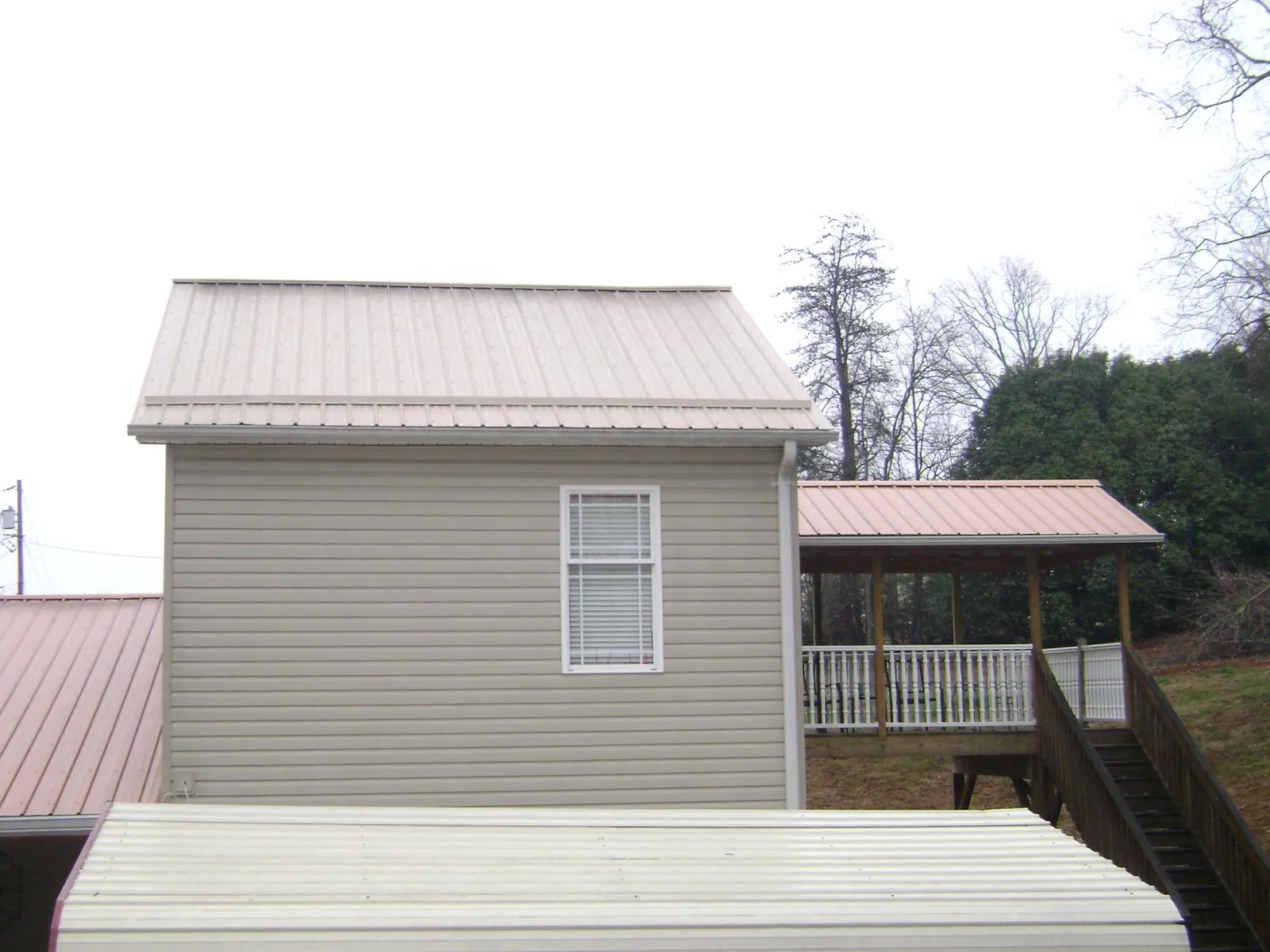 Tan metal roofs on a two story addition and attached porch, from a Roof Replacement job in Syria